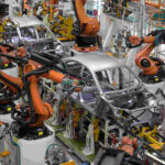 : Advanced robotic arms in a car manufacturer automation systems line assembling an electric vehicle chassis.