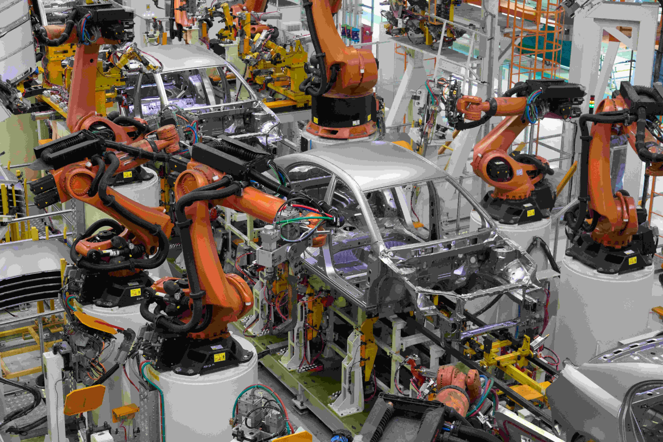 : Advanced robotic arms in a car manufacturer automation systems line assembling an electric vehicle chassis.